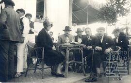 Tarjeta postal con fotografía de Jesús Guridi sentado a una mesa en una terraza con otros cuatro hombres y su mujer.